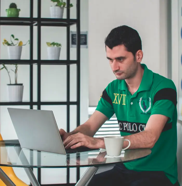 Młody mężczyzna w T-shircie siedzi przy szklanym stoliku i pisze coś na laptopie